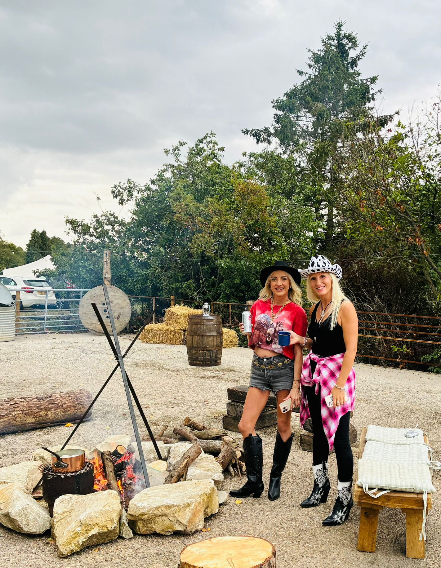 Two colleagues in cowboy hats and boots, drinks in hand, beside the campfire in the Branding Pen