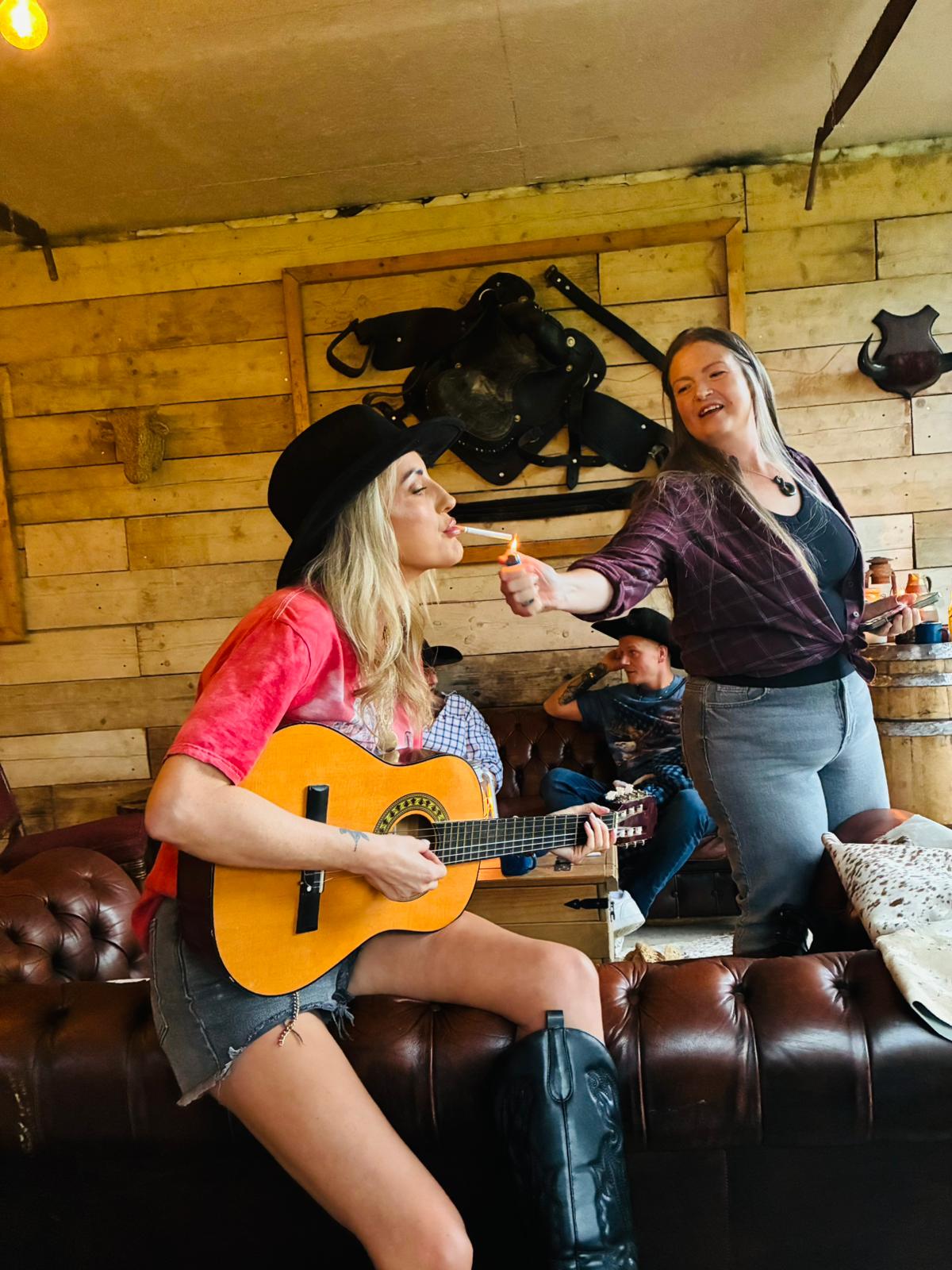 Someone strumming an acoustic guitar on the saloon sofa while the rest of the team looks on